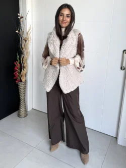 Mujer con chaleco de pelo beige, posando de forma natural con una mano en el cabello.