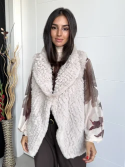 Mujer con chaleco pelo sintético beige claro, corte recto y largo a la cadera, de pie con pantalón marrón.