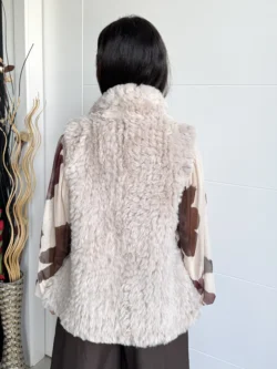 Mujer mostrando la espalda del chaleco beige de pelo sintético, corte recto hasta la cadera.