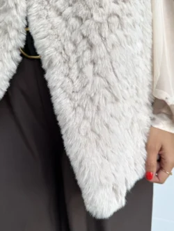 Primer plano del chaleco beige de pelo sintético, mostrando broche de cierre oculto en la parte delantera.