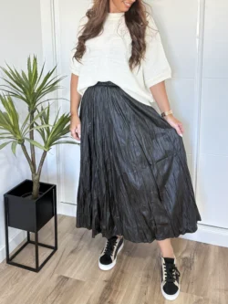 Mujer con falda midi polipiel negra combinada con jersey blanco y zapatillas.