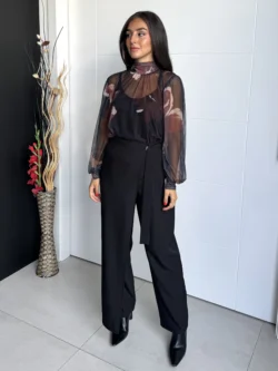 Mujer con blusa floral semitransparente negra y pantalón de vestir negro, de cuerpo entero
