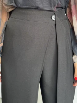 Detalle de cinturilla cruzada con botón en pantalón negro de tiro alto.