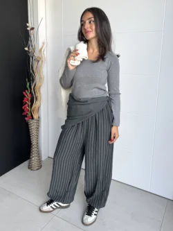 Mujer con pantalón fluido a rayas gris y jersey gris, look casual con deportivas.