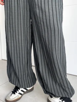 Bajo del pantalón fluido gris con rayas negras, combinado con zapatillas deportivas.