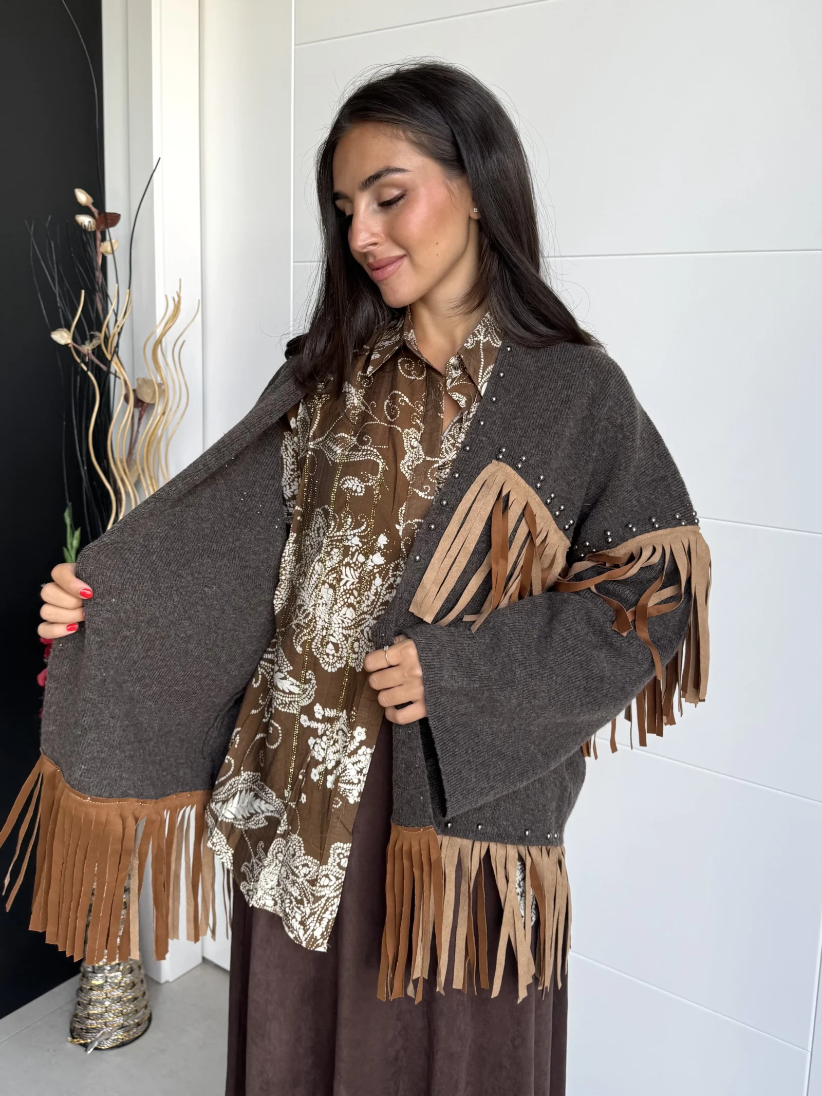 Mujer mostrando chaqueta marrón abierta con flecos sobre blusa estampada.
