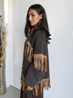Mujer en perfil luciendo chaqueta marrón oversize con flecos en mangas y bajo.