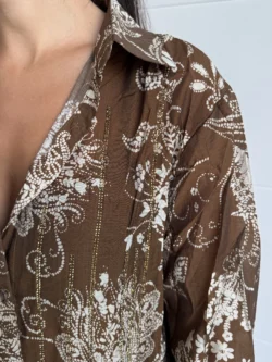 Primer plano del cuello y hombro de camisa marrón con estampado floral y líneas doradas.