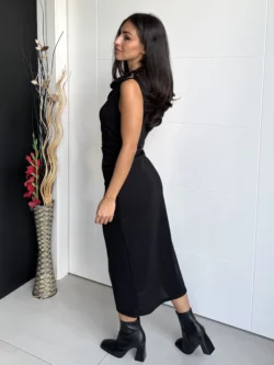 Mujer con vestido negro ajustado y broches dorados, vista de perfil.