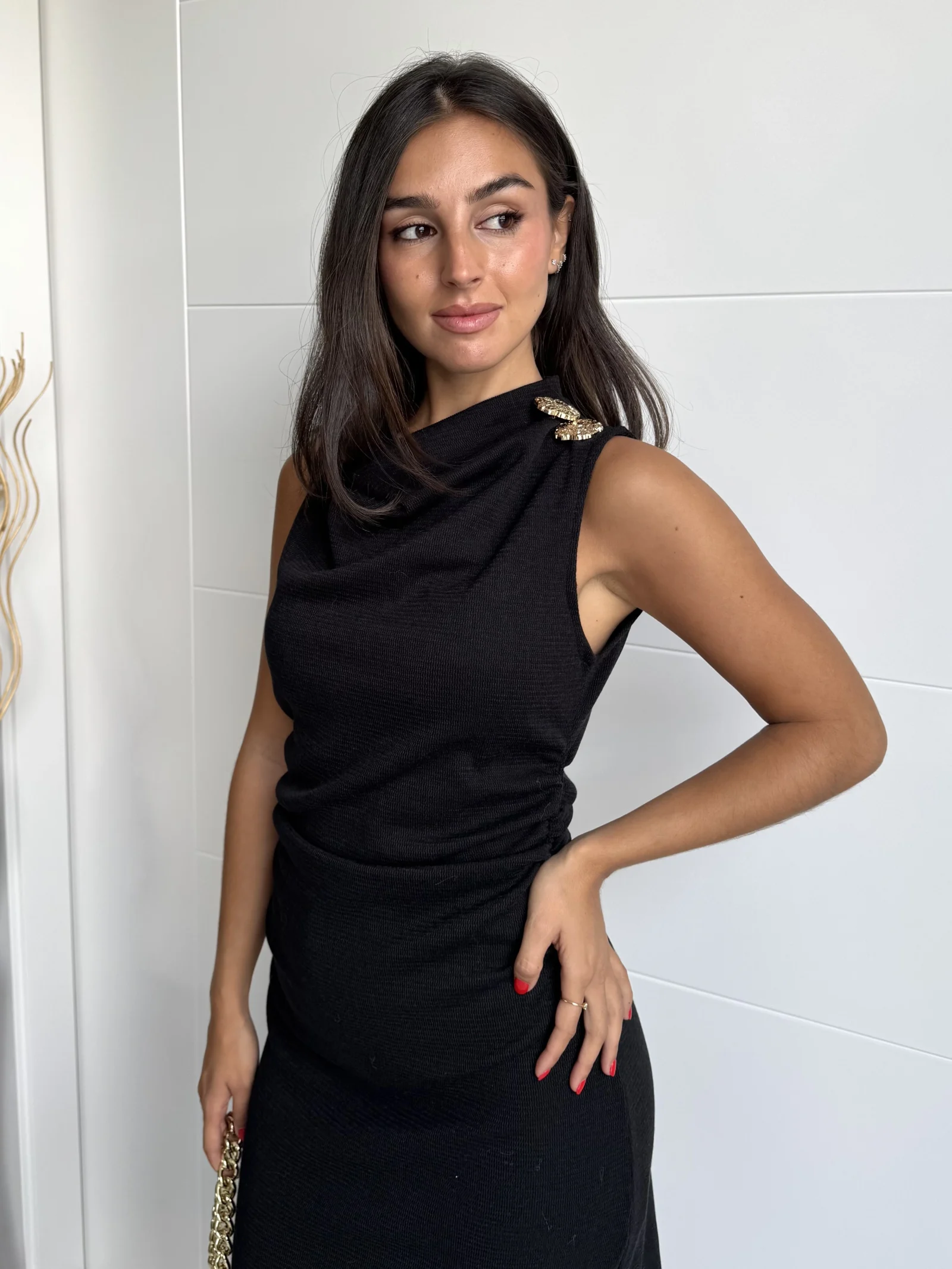 Mujer con vestido negro entallado de punto y broches dorados en los hombros.
