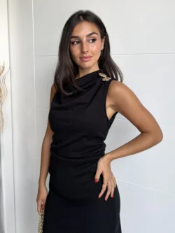 Mujer con vestido negro entallado de punto y broches dorados en los hombros.