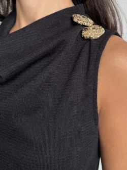 Primer plano del broche dorado decorativo en hombro de vestido negro.